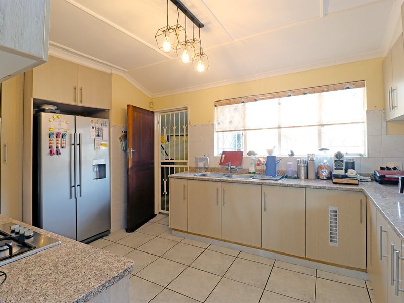 Functional kitchen featuring light-toned cabinetry, granite countertops, tiled flooring, and a gas hob, with direct access to an external security gate.