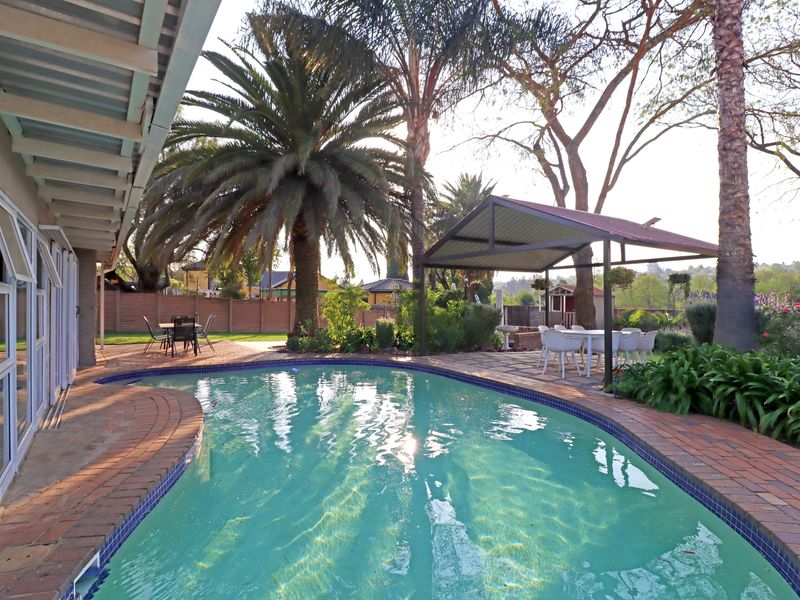 Outdoor pool area featuring a swimming pool with brick coping and a covered patio structure, set within a landscaped garden.