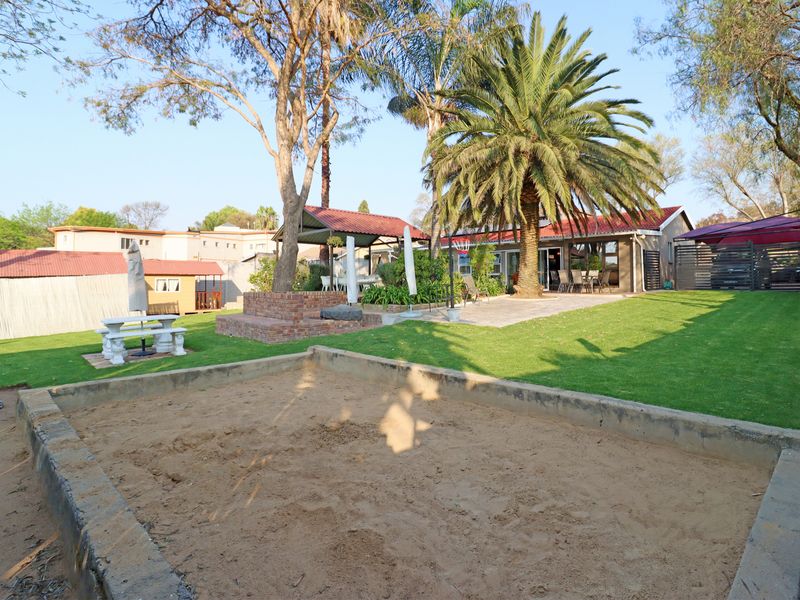 Spacious rear garden featuring a large sandpit, manicured lawn, paved patio area, and a covered pergola, ideal for outdoor family recreation.