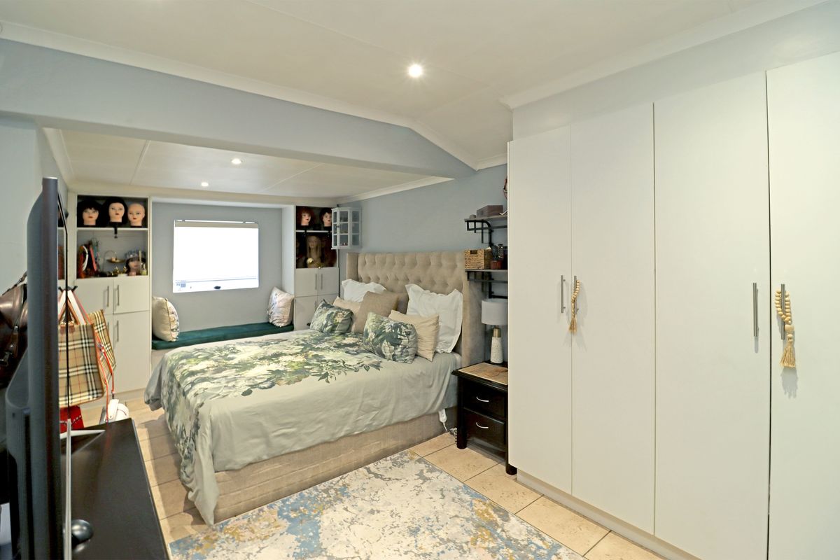 A well-lit bedroom featuring built-in cupboards, a cozy window seat, and tiled flooring, offering a functional and comfortable living space.