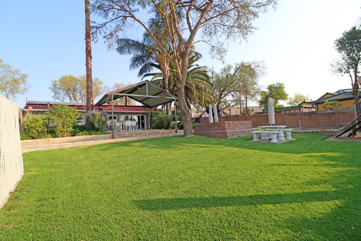 Spacious rear garden featuring a well-maintained lawn, mature trees, a covered patio area, and a brick built-in braai, perfect for outdoor entertaining.