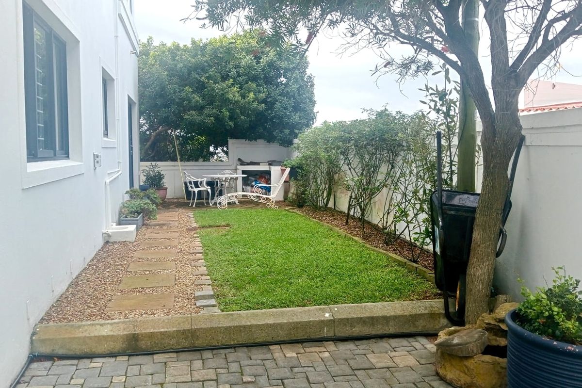 A private rear garden featuring a paved walkway, a well-maintained lawn, and a built-in braai area enclosed by boundary walls.