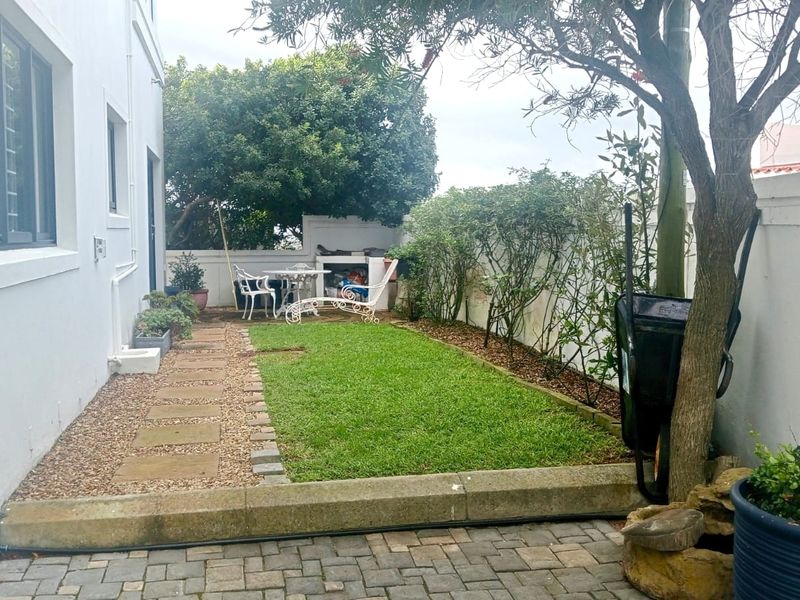 A private rear garden featuring a paved walkway, a well-maintained lawn, and a built-in braai area enclosed by boundary walls.