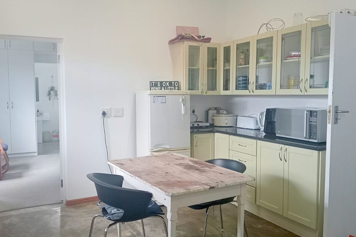 A functional kitchen featuring light-toned cabinetry, granite countertops, and glass-fronted upper storage, providing a practical workspace with direct access to an adjacent room.