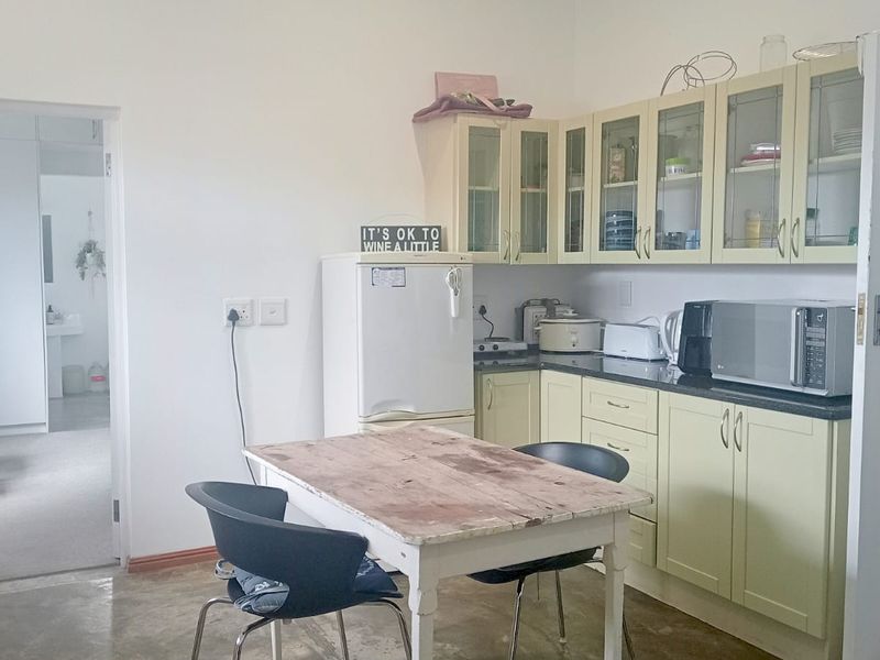 A functional kitchen featuring light-toned cabinetry, granite countertops, and glass-fronted upper storage, providing a practical workspace with direct access to an adjacent room.