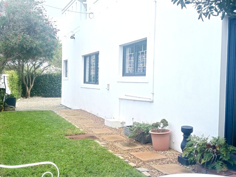 A view of the rear exterior of the townhouse, featuring a paved walkway, manicured lawn, and secure window fittings.