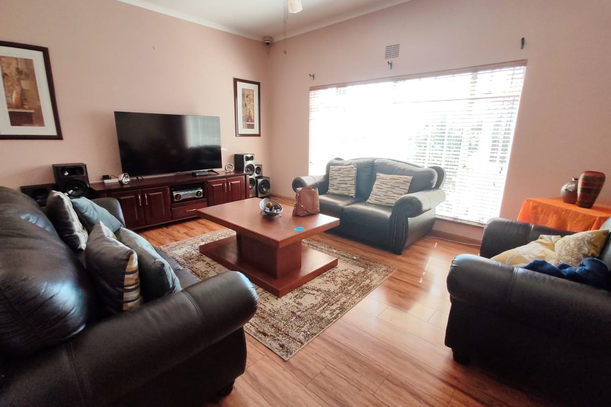 A comfortable living room featuring laminate flooring, a ceiling fan, and large windows with venetian blinds, providing a functional and well-lit space.