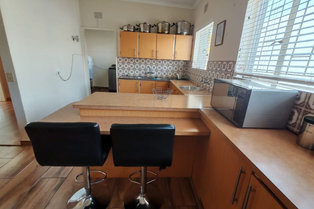 A functional kitchen featuring laminate cabinetry, a breakfast bar, tiled backsplash, and double sink, offering a dated but well-maintained layout.