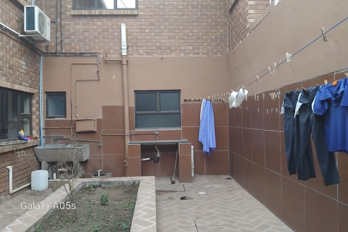 A functional rear utility courtyard featuring a concrete wash basin, tiled walls, and paved flooring, suitable for laundry or outdoor maintenance tasks.