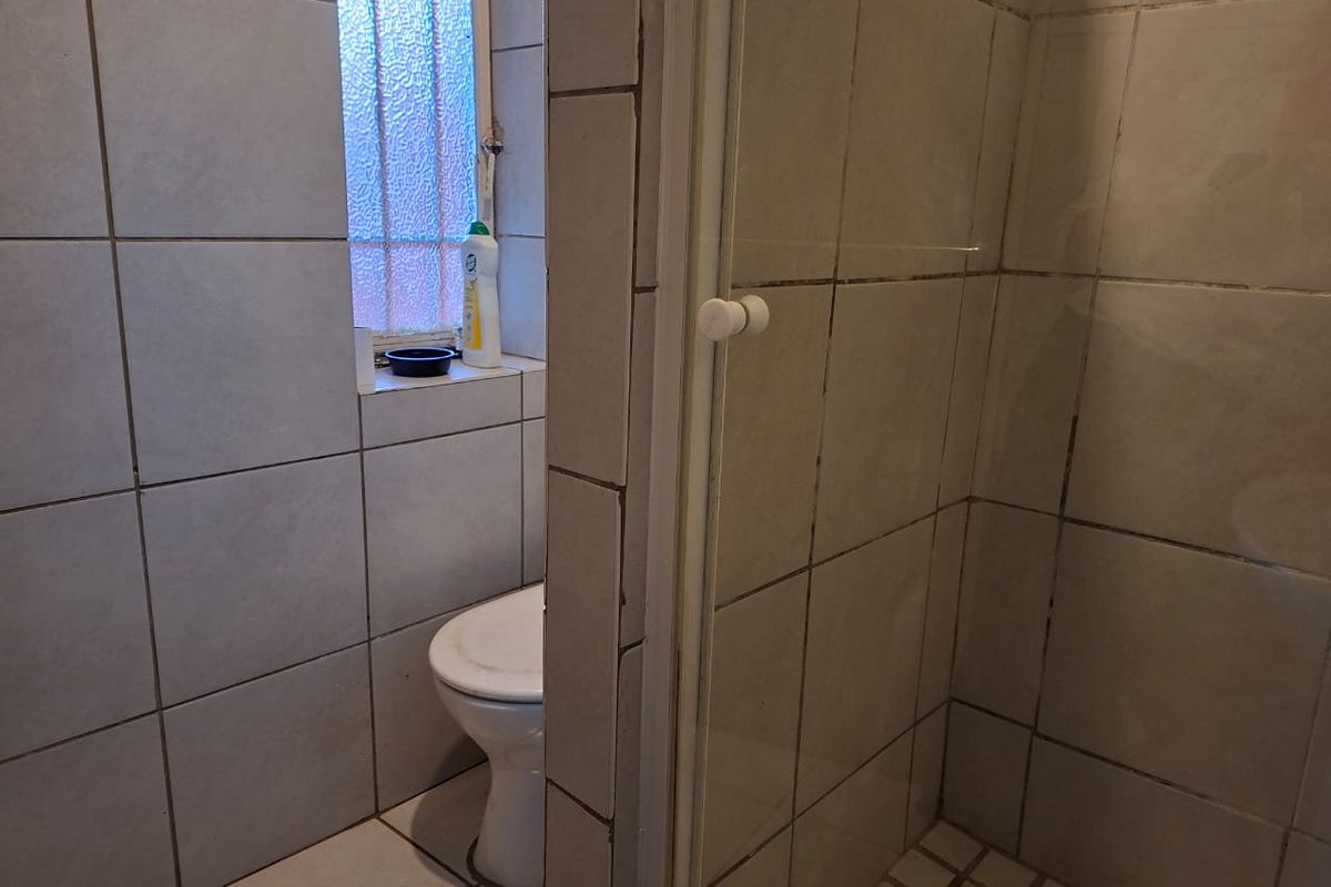A compact bathroom featuring a tiled shower enclosure and a separate toilet area with a privacy window.