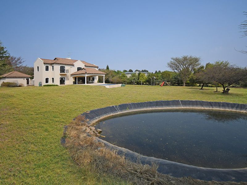 Rear view of a multi-story residential property featuring a covered patio, swimming pool, and a large garden with a dam.