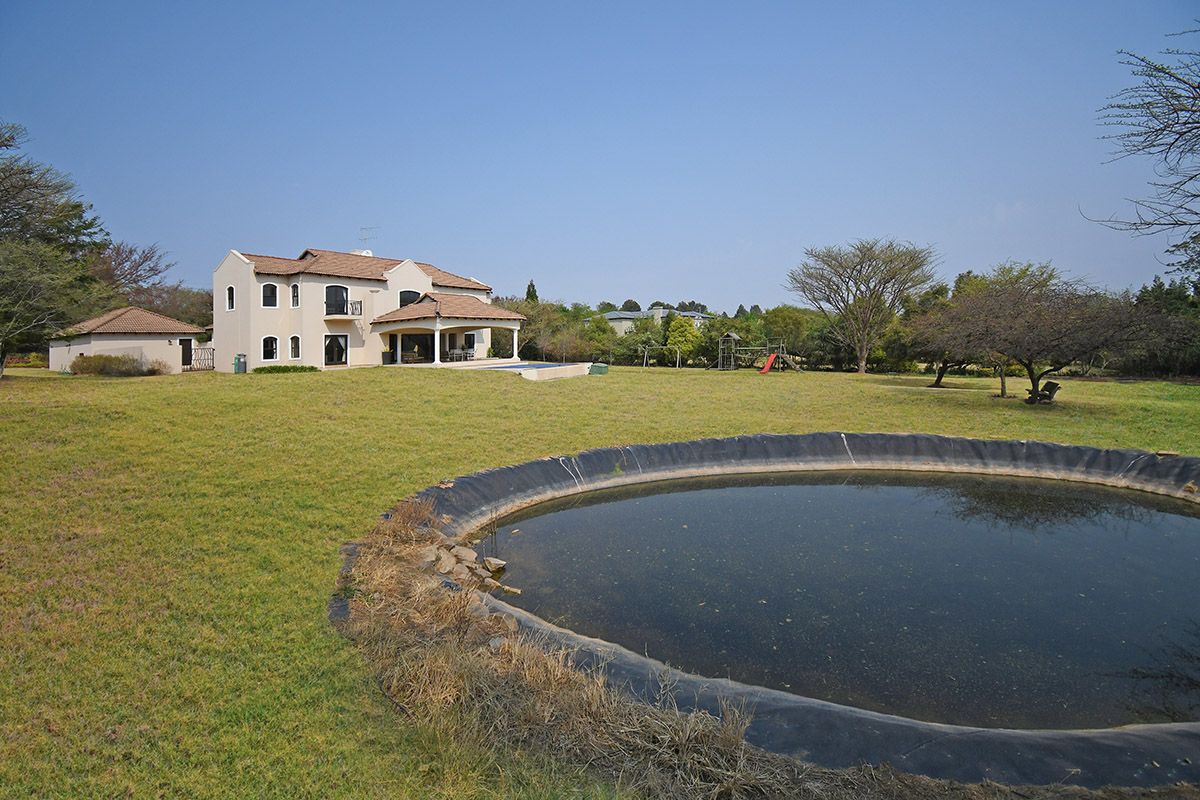 Rear view of a multi-story residential property featuring a covered patio, swimming pool, and a large garden with a dam.