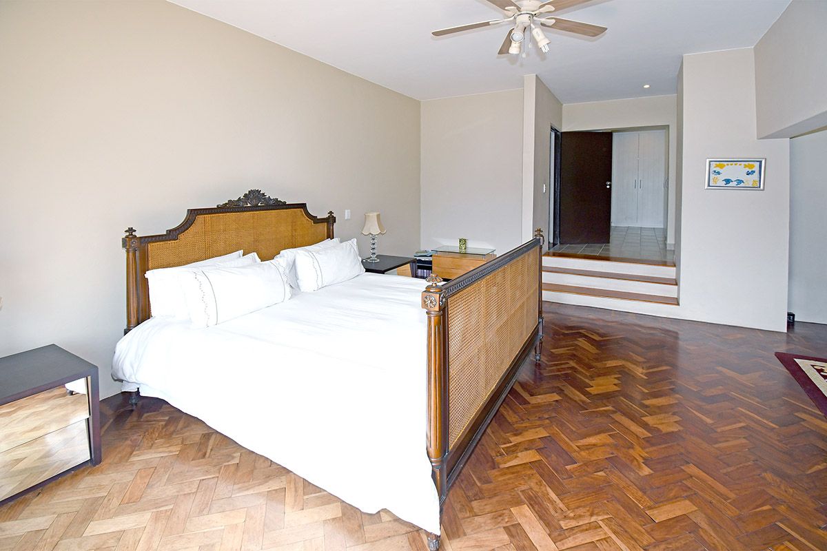 Spacious bedroom featuring classic herringbone parquet flooring, a ceiling fan, and a raised platform leading to a separate dressing area with built-in cupboards.