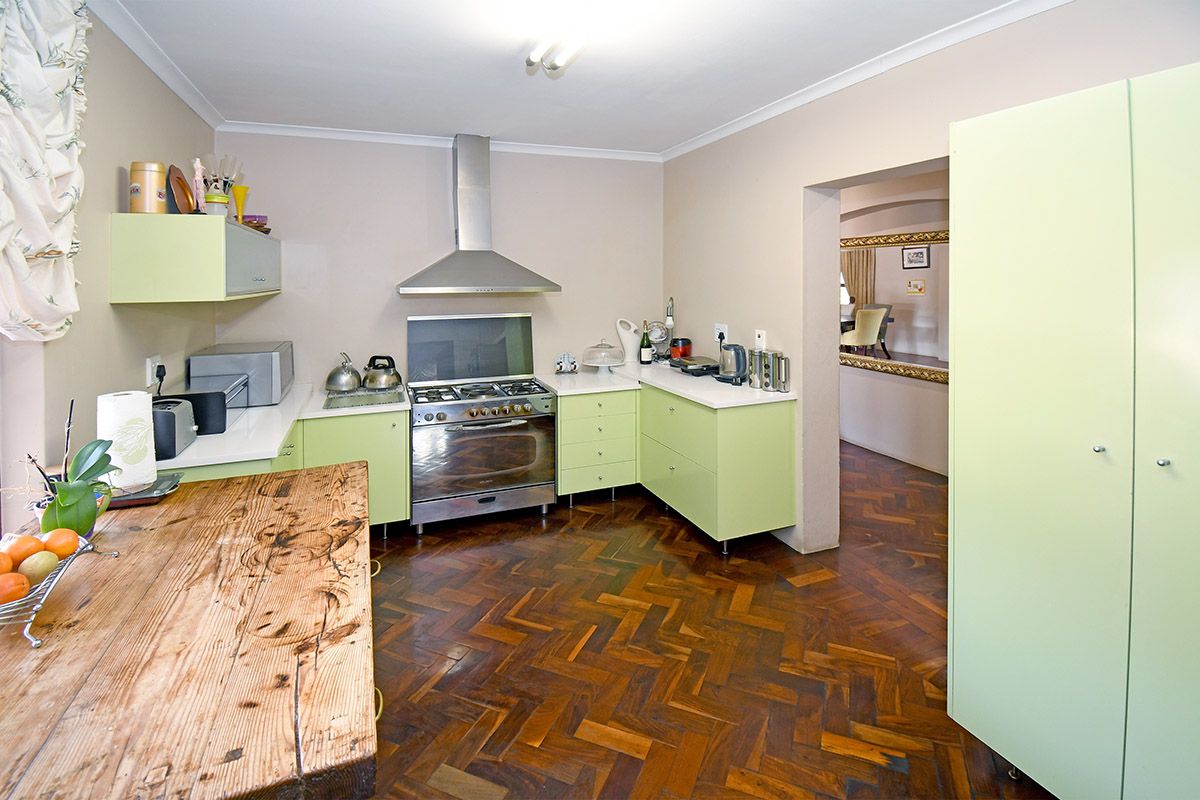 A functional kitchen featuring light green cabinetry, a stainless steel gas stove with extractor fan, and classic parquet flooring.