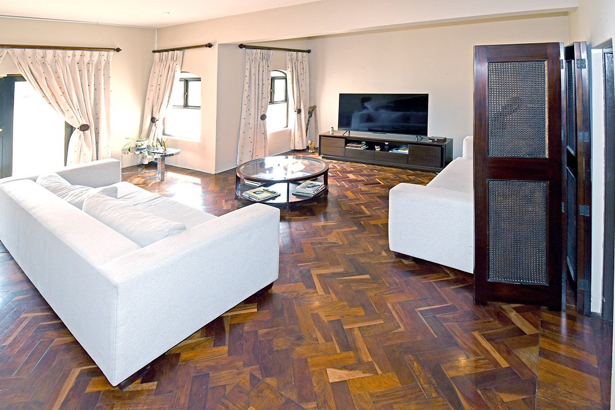 Spacious living room featuring classic herringbone parquet flooring, neutral walls, and large windows allowing for ample natural light.