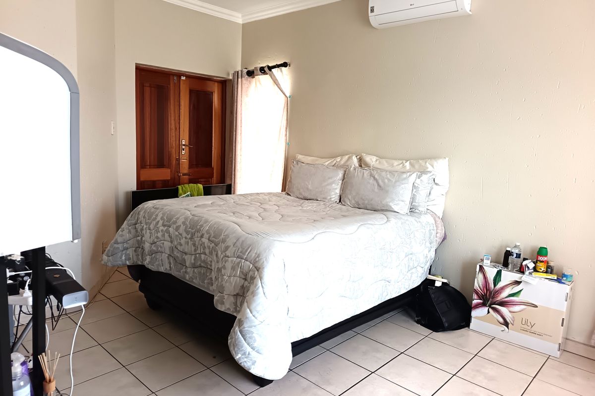 A bedroom featuring tiled flooring, a wall-mounted air conditioning unit, and wooden double doors leading to an adjacent space.