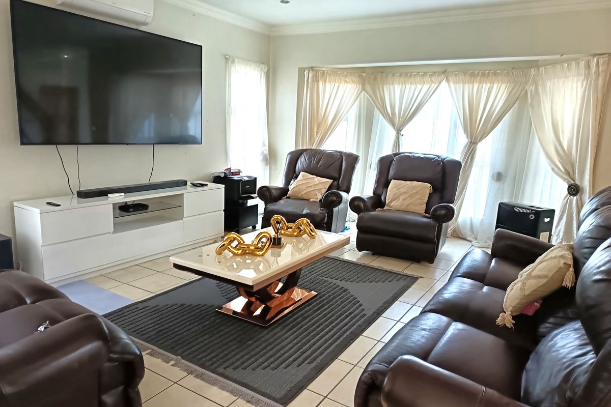A comfortable living room featuring tiled flooring, recessed ceiling lighting, and a large bay window with curtains.