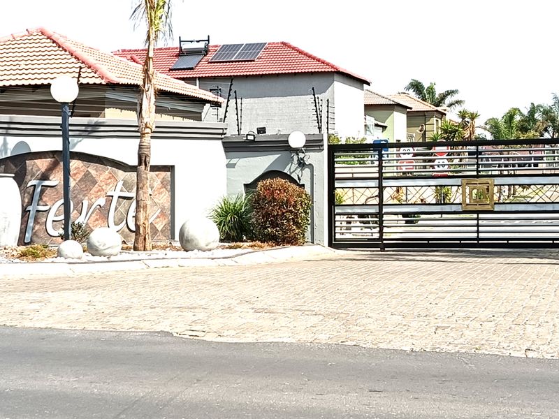 The entrance to the property features a paved driveway, a secure metal gate, and a decorative wall with integrated lighting and solar panels.