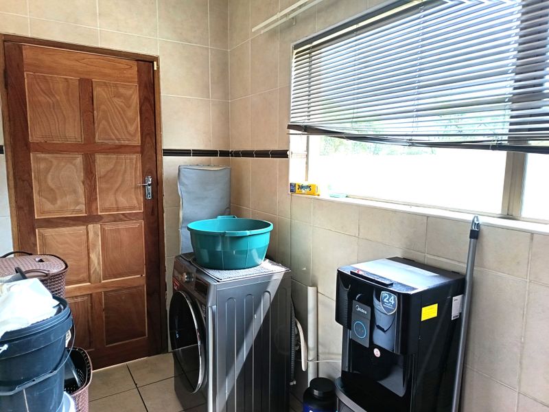 A functional laundry room featuring tiled walls, a window with blinds, and dedicated space for laundry appliances.