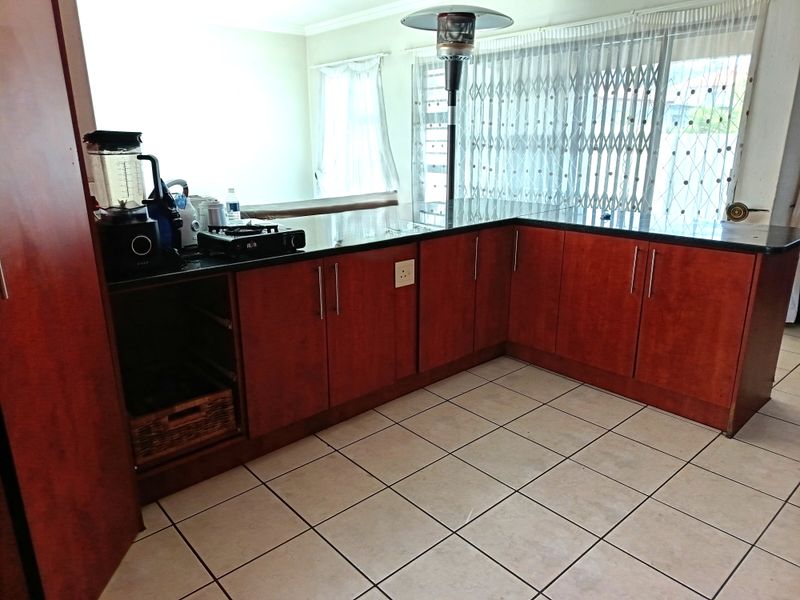 A functional kitchen featuring dark wood-finish cabinetry, black granite countertops, and light-colored ceramic floor tiles with a breakfast bar area.