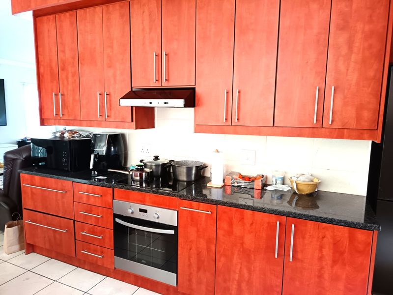 A functional kitchen featuring cherry-toned cabinetry, black granite countertops, a built-in oven, and a stainless steel extractor fan.