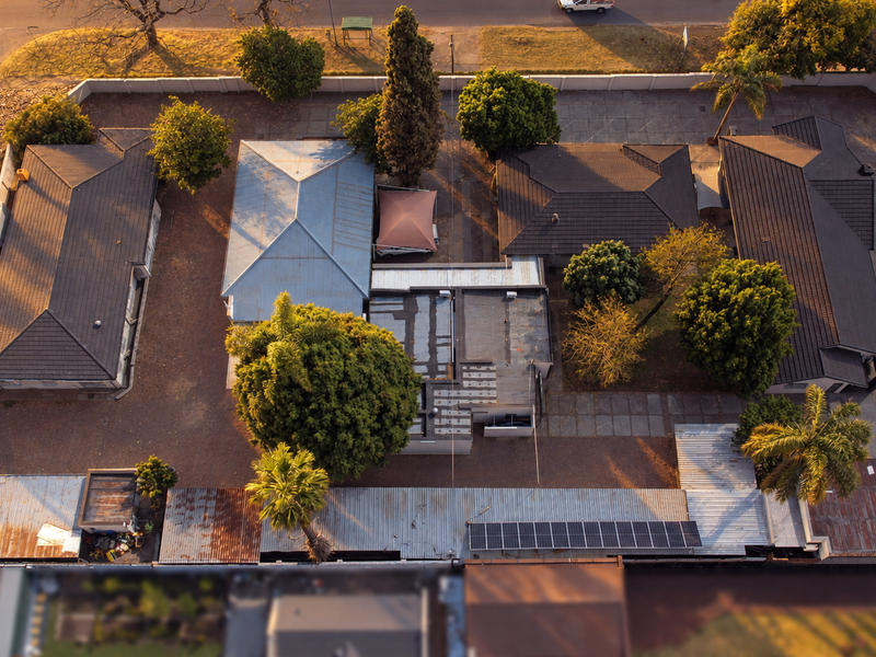 Aerial view of the property showing multiple building structures, tiled and metal roofing, solar panels, and a paved courtyard area.