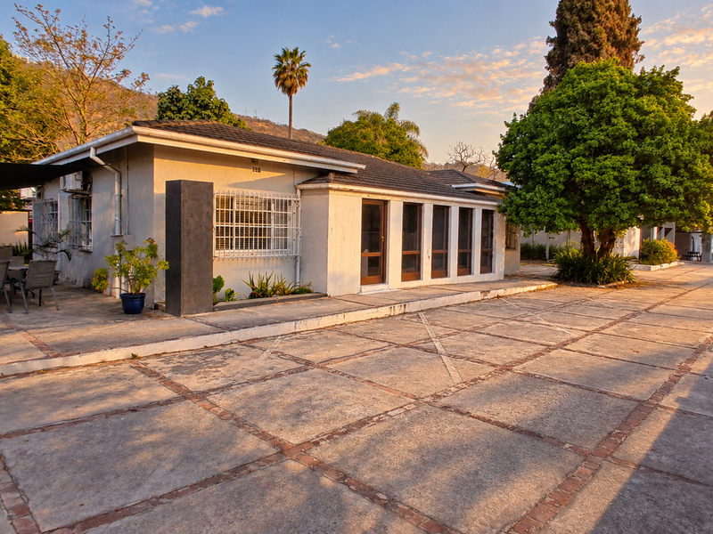 A spacious rear exterior view featuring a large paved patio area, tiled roof, and secure window fixtures set against a landscaped garden backdrop.