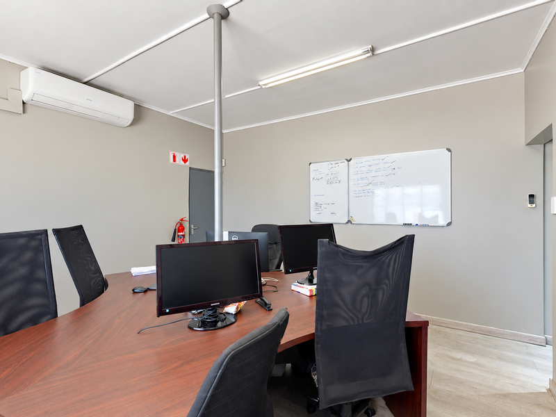 A functional office space featuring built-in storage cupboards, a split-system air conditioner, and neutral wall finishes, suitable for a professional work environment.