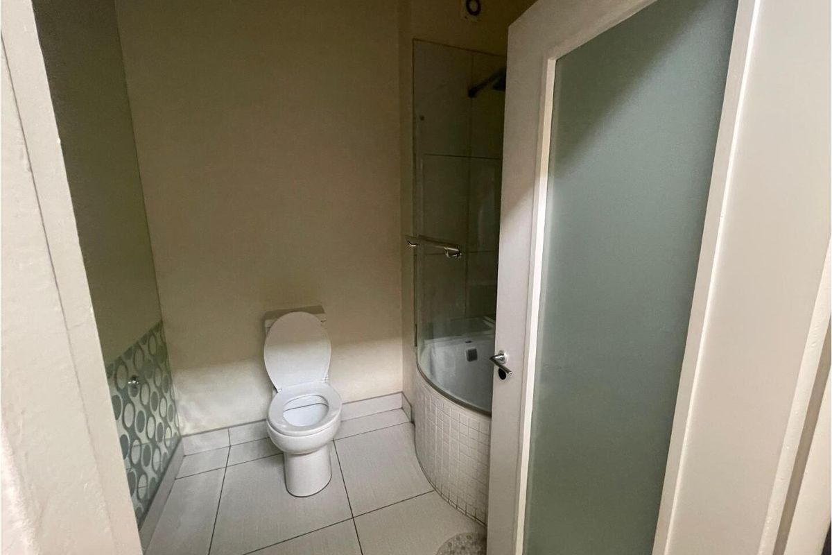 A compact bathroom featuring a white toilet, a curved glass shower enclosure with tiled base, and neutral floor tiling.