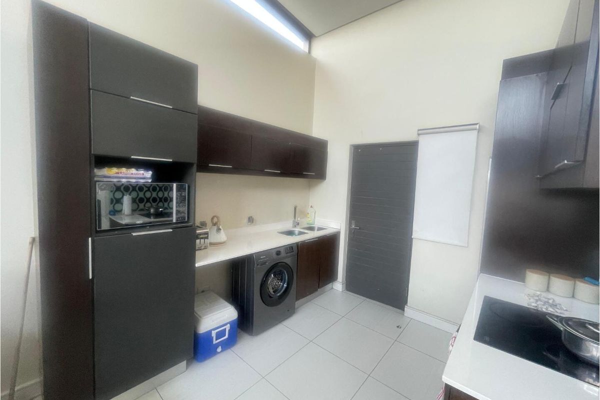A functional kitchen featuring dark cabinetry, white countertops, integrated appliances, and tiled flooring with high ceilings and natural light.