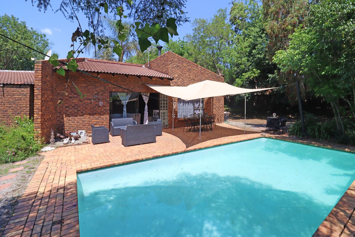 Rear exterior view featuring a brick house, a paved patio area, and a swimming pool set within a mature garden.