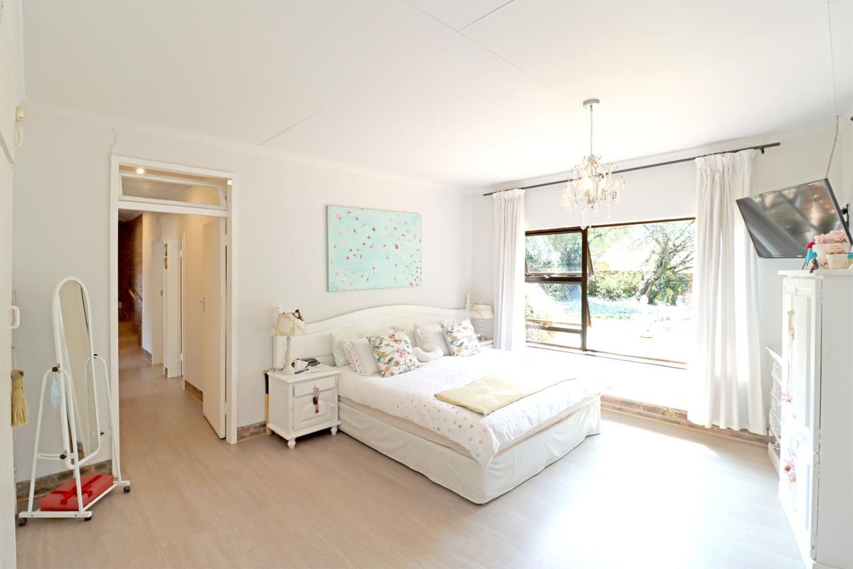 A bright and spacious bedroom featuring large windows with garden views, neutral flooring, and a classic chandelier fixture.