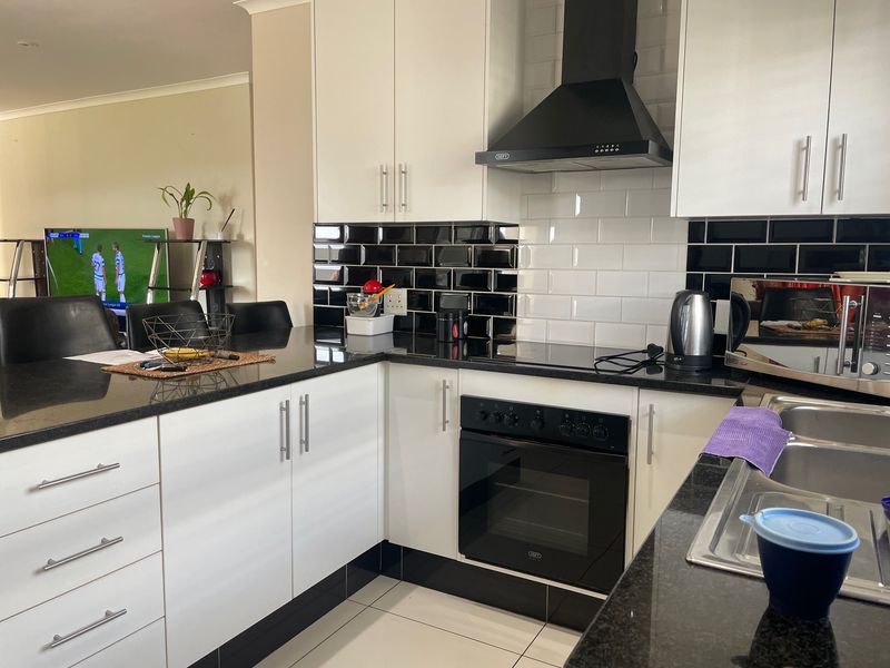 Modern kitchen featuring white cabinetry, black granite countertops, subway tile backsplash, and integrated appliances including an oven, hob, and extractor fan.