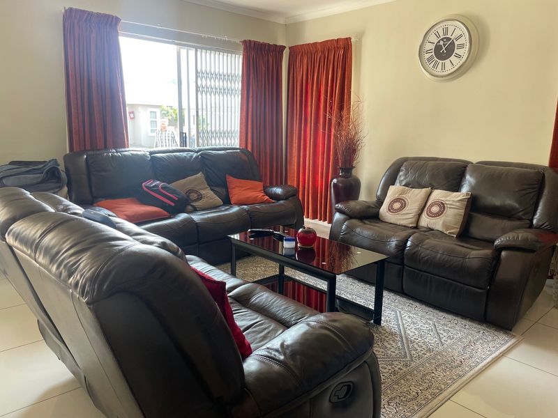 A comfortable living room featuring tiled flooring, a sliding glass door with security gate, and neutral wall finishes.