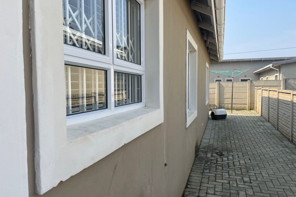 A side exterior view of the townhouse featuring paved pathways, security-fitted windows, and a precast concrete boundary wall.