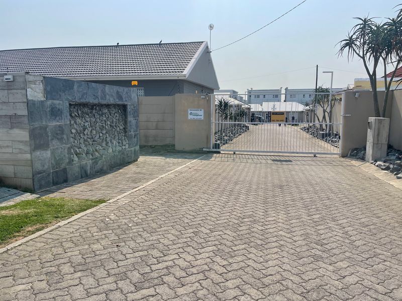 View of the townhouse complex entrance featuring a paved driveway, secure gated access, and a decorative stone-clad perimeter wall.