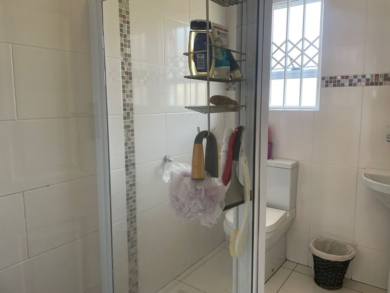A functional bathroom featuring a shower enclosure, pedestal basin, toilet, and white wall tiles with a decorative mosaic border.