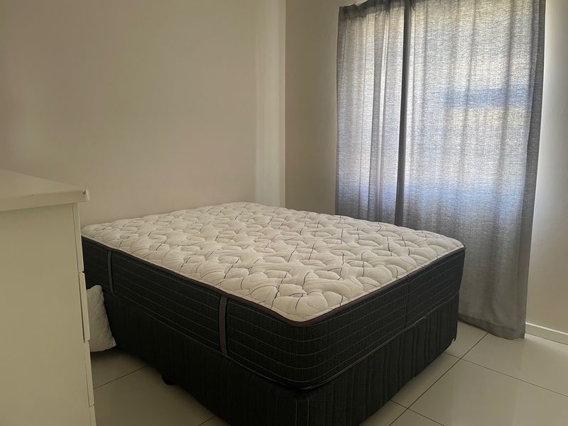 A simple bedroom featuring neutral wall finishes, tiled flooring, and window curtains.
