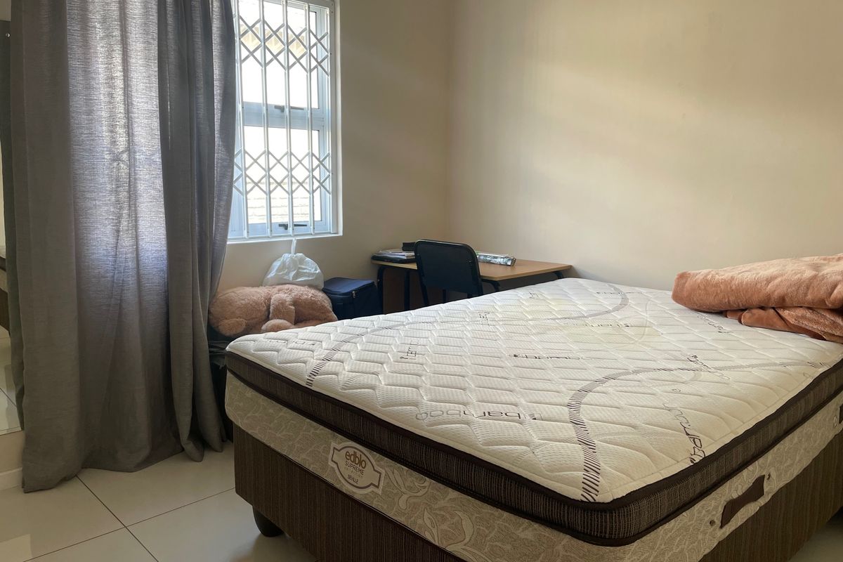 A functional bedroom featuring tiled flooring and a window fitted with security bars, providing a basic and practical living space.
