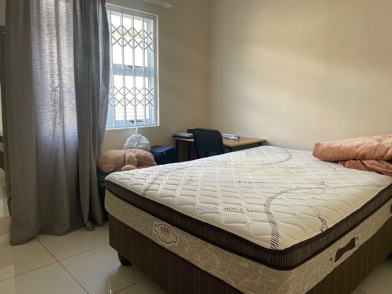 A functional bedroom featuring tiled flooring and a window fitted with security bars, providing a basic and practical living space.