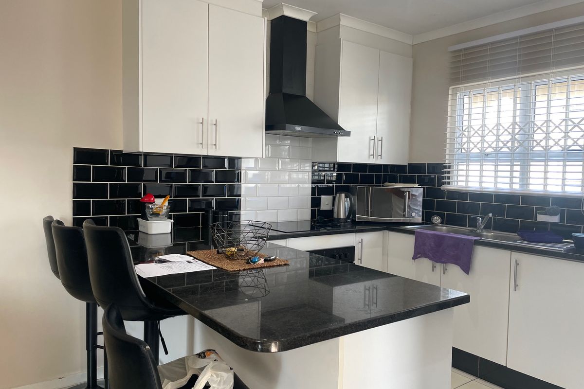 Modern kitchen featuring sleek white cabinetry, contrasting black subway tile backsplash, granite countertops, and a breakfast bar area with integrated extractor fan.