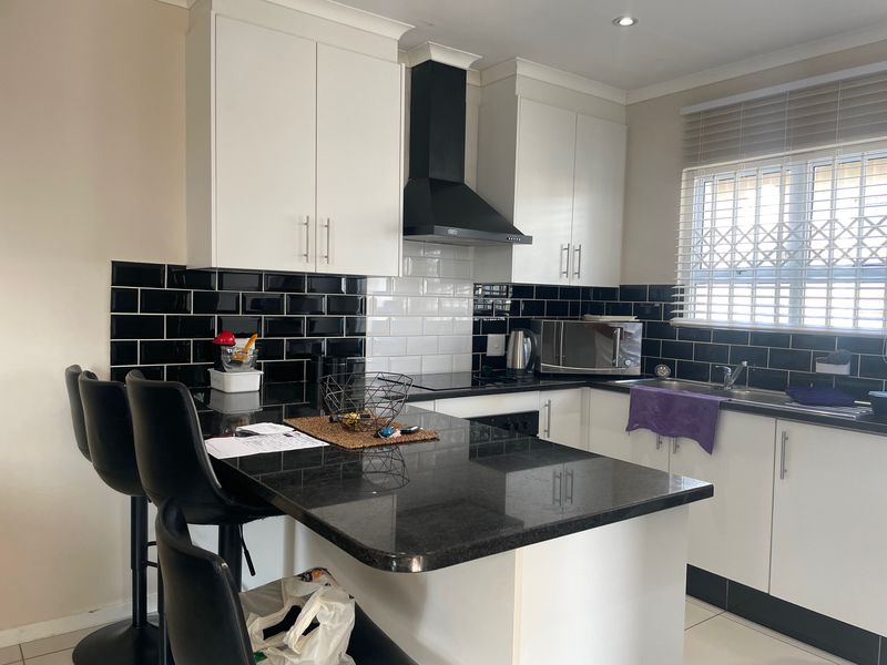 Modern kitchen featuring sleek white cabinetry, contrasting black subway tile backsplash, granite countertops, and a breakfast bar area with integrated extractor fan.