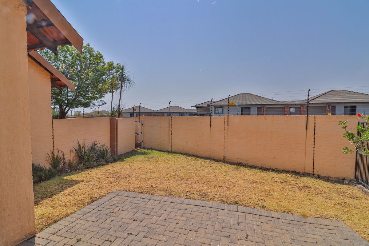 A private rear garden featuring a paved patio area, enclosed by a perimeter wall with electric fencing.