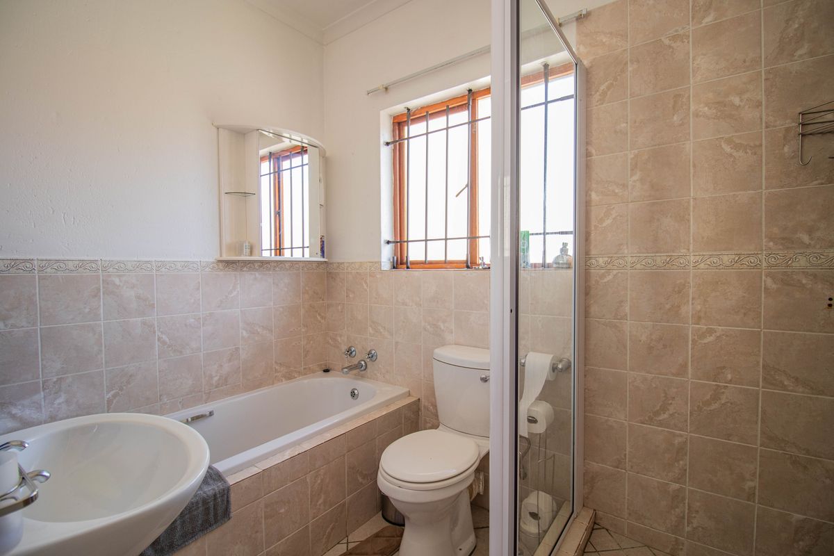 A functional bathroom featuring a bathtub, separate shower enclosure, toilet, and basin with neutral wall tiling and window security bars.