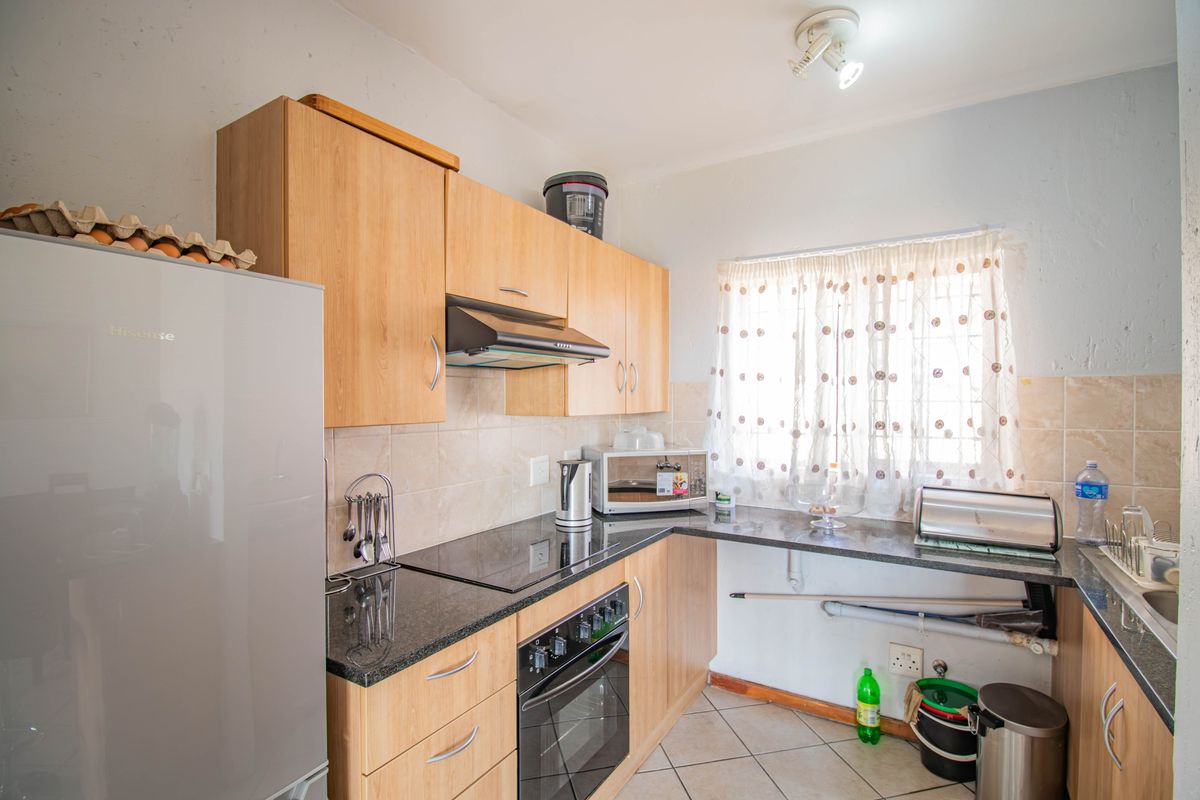 Functional kitchen featuring light wood cabinetry, granite countertops, built-in oven, electric hob, and tiled backsplash with a window overlooking the exterior.
