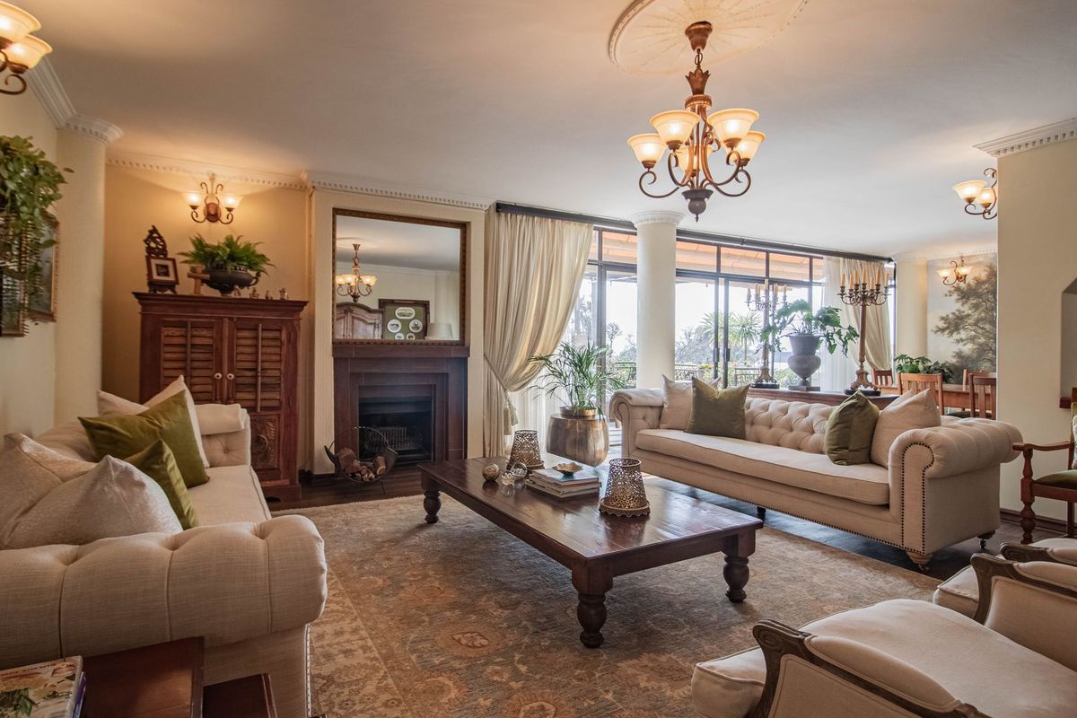Spacious living room featuring a classic fireplace, decorative ceiling rose, elegant chandelier lighting, and large glass sliding doors leading to an outdoor patio area.