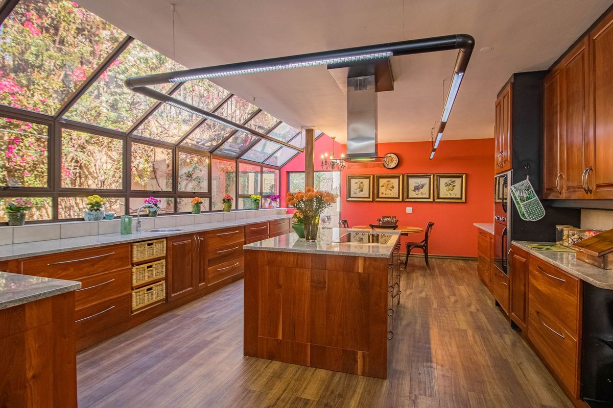 Spacious kitchen featuring custom wood cabinetry, granite countertops, a central island with integrated cooktop, and a striking glass-enclosed conservatory-style wall.
