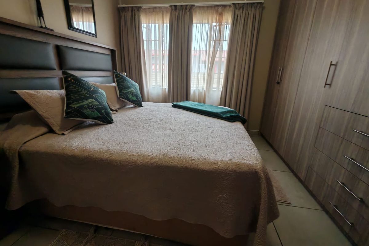 A well-maintained bedroom featuring built-in wooden wardrobes, tiled flooring, and large windows with curtains, providing a comfortable and functional living space.
