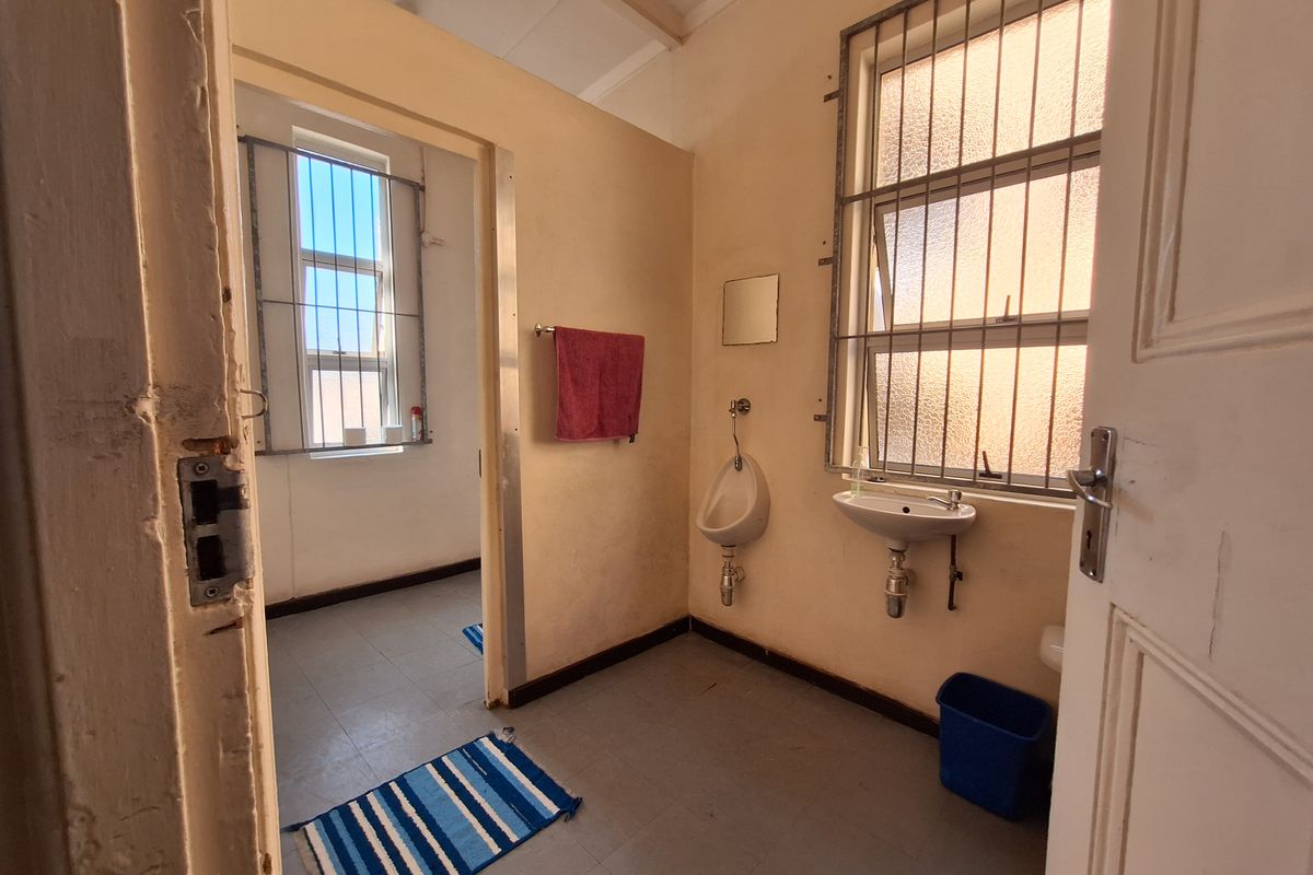 A functional bathroom featuring a wall-mounted urinal and basin, with security bars on the windows and tiled flooring.