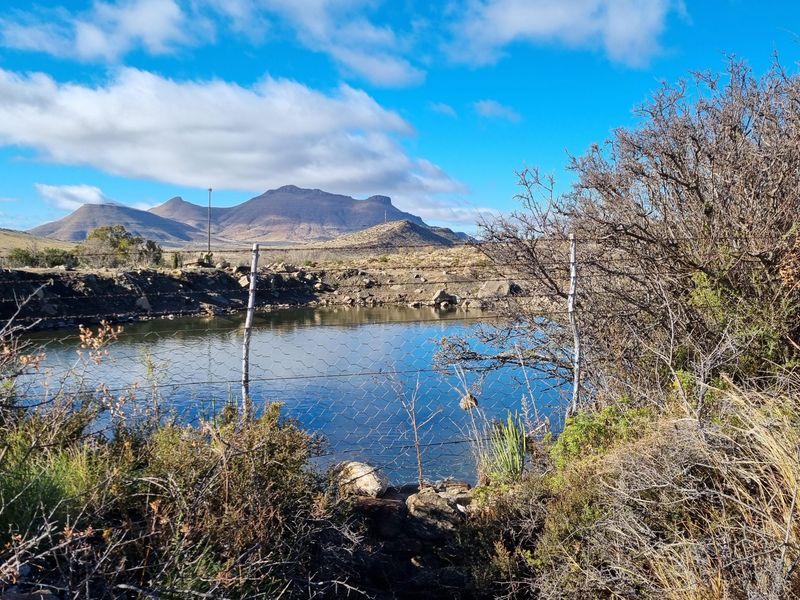 A scenic view of a farm dam with mountain vistas, featuring natural landscape and perimeter wire fencing.